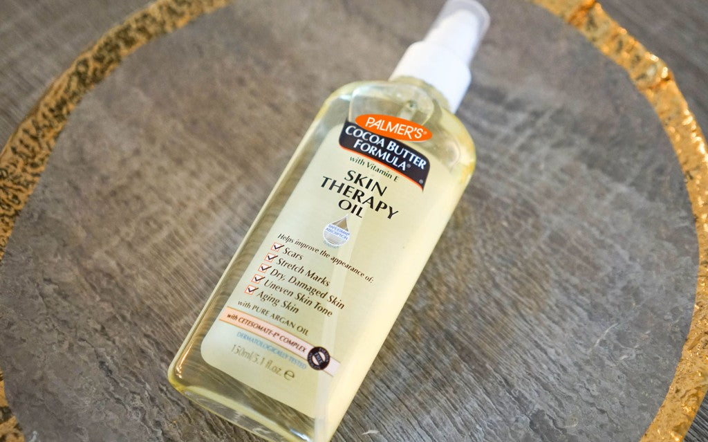 One of the best oils for skin repair and damaged skin, Palmer's Skin Therapy Oil in carved gold ring on wooden table