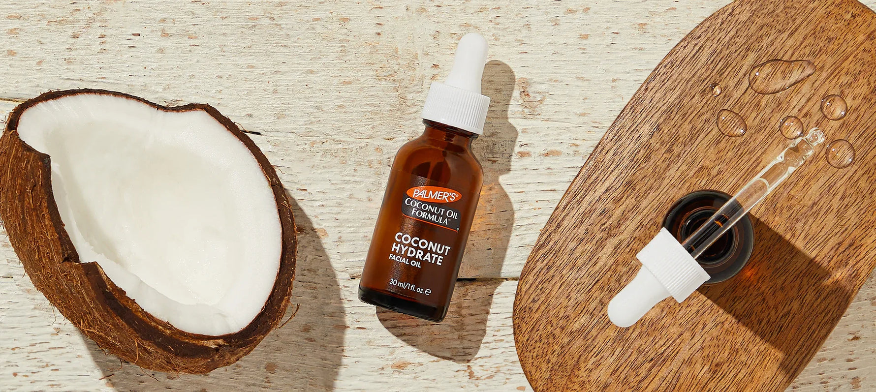 Palmer's Coconut Hydrate Facial Oil on wooden table with open bottle and dropper and half a coconut