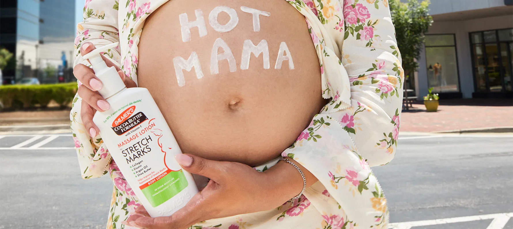 Pregnant woman with Hot Mama written on belly holding bottle of Palmer's Massage Lotion for Stretch Marks