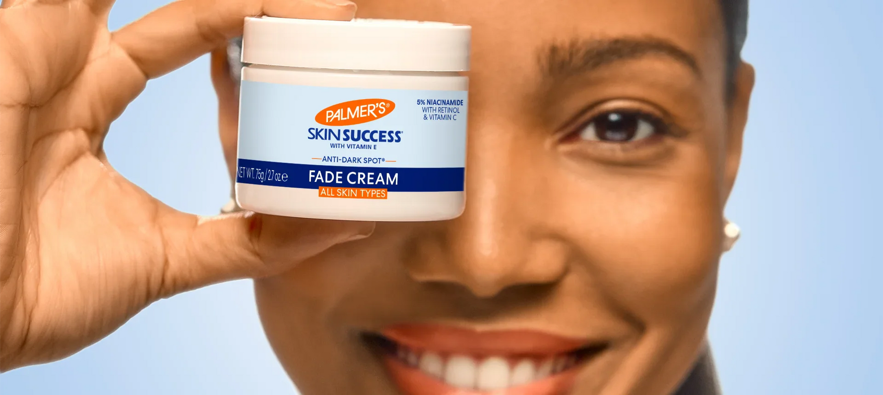 Close up of woman holding jar of Palmer's Skin Success Fade Cream in front of her eye