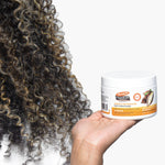 Hand holding Cocoa Butter Deep Conditioner beside curly hair.