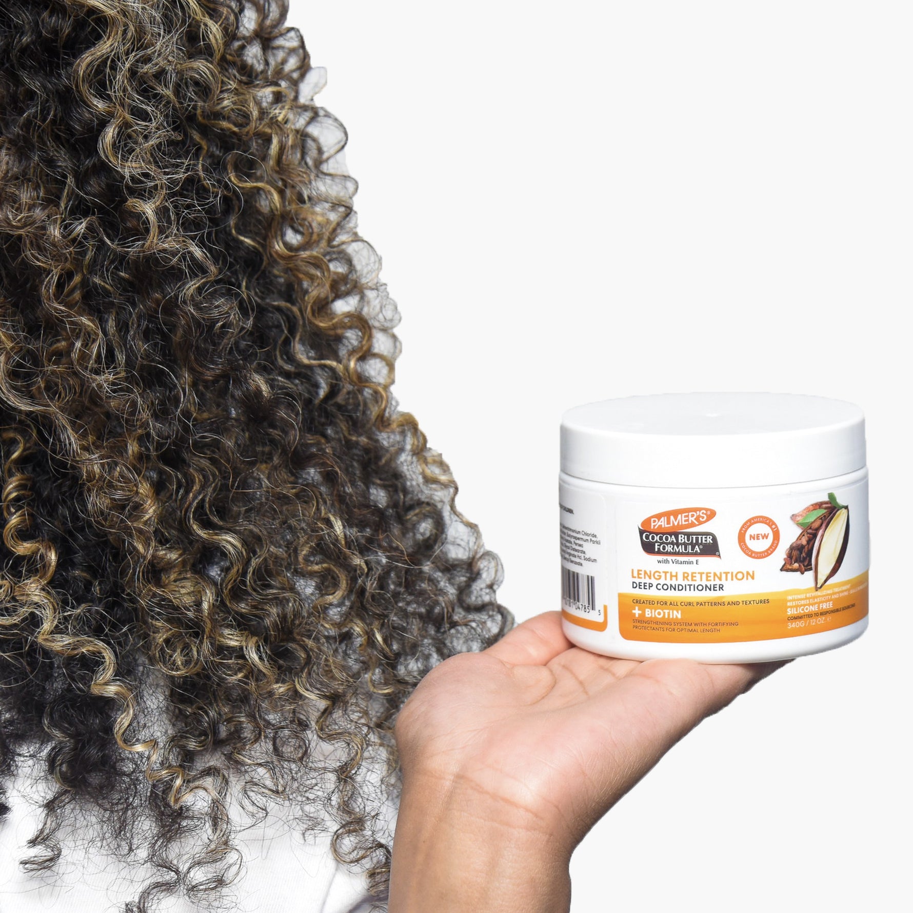 Hand holding Cocoa Butter Deep Conditioner beside curly hair.