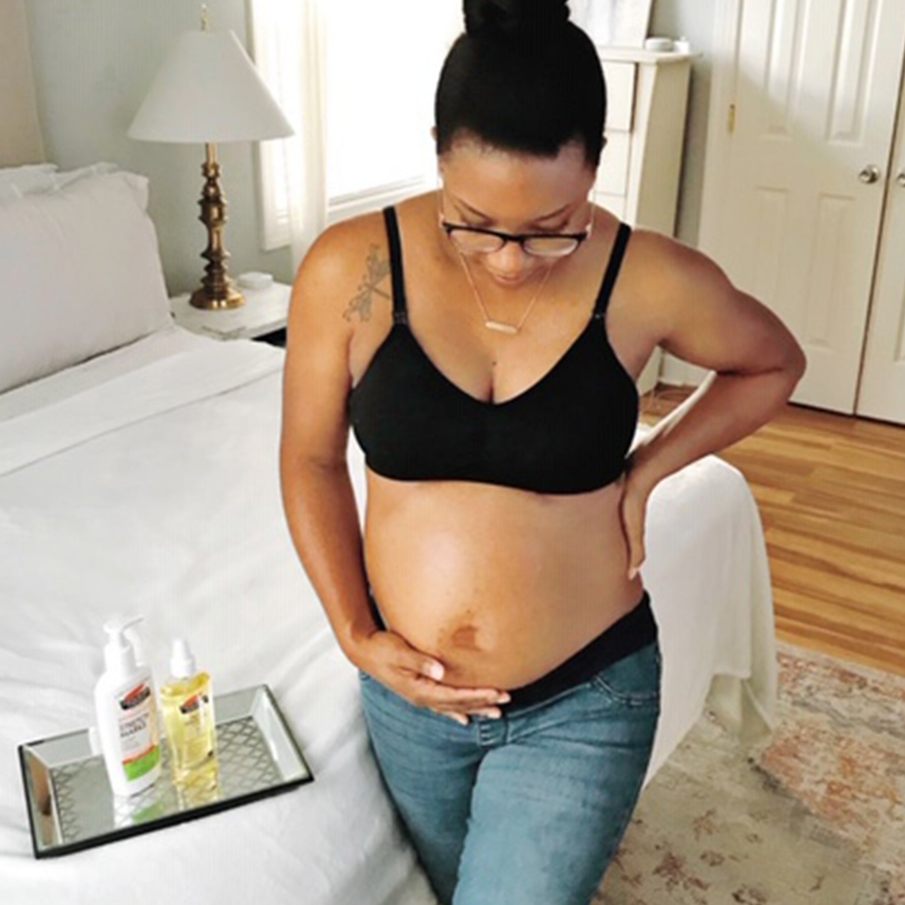 Person holding midriff beside bed with Cocoa Butter Skin Therapy Oil.