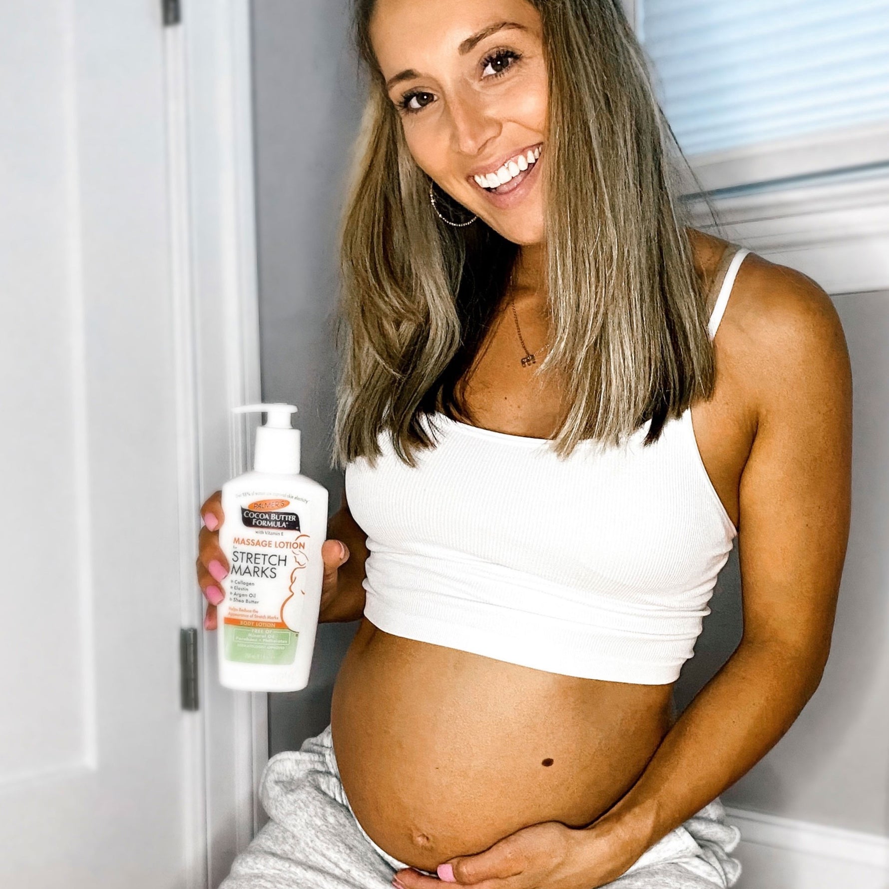 Pregnant woman holding Palmer's Mommy To Be Kit lotion bottle.