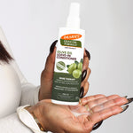 Hands dispensing Palmer’s Olive Oil Leave-In Conditioner for shine therapy.