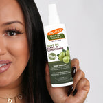 Woman holding Palmer’s Olive Oil Leave-In Conditioner spray bottle.