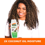 Person smiling, holding Palmer’s Coconut Oil Shampoo, emphasizing moisture boost.