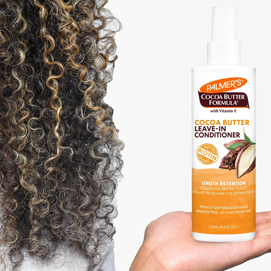 Palmer's Cocoa Butter Formula leave-in conditioner bottle held by a hand next to curly hair.