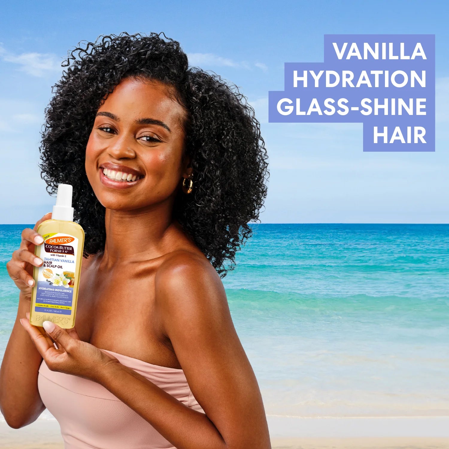 Woman holding a bottle of Palmers Cocoa Butter Formula Tahitian Vanilla Hair & Scalp Oil on a beach with text 'Vanilla Hydration Glass-Shine Hair'.