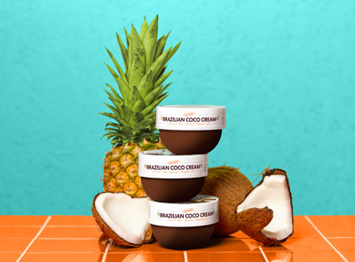 Palmer's Brazilian Coco Cream jars, one of the top ways how to reduce cellulite, stacked on tiles with coconut and pineapple