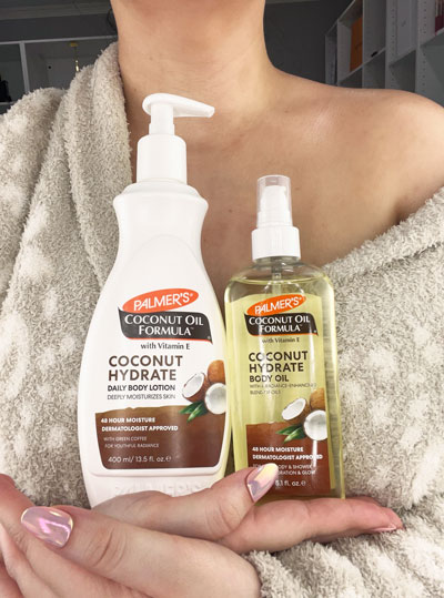 Woman in robe holding Palmer's hydrating skin care Coconut Oil Body Lotion and Coconut Oil Body Oil