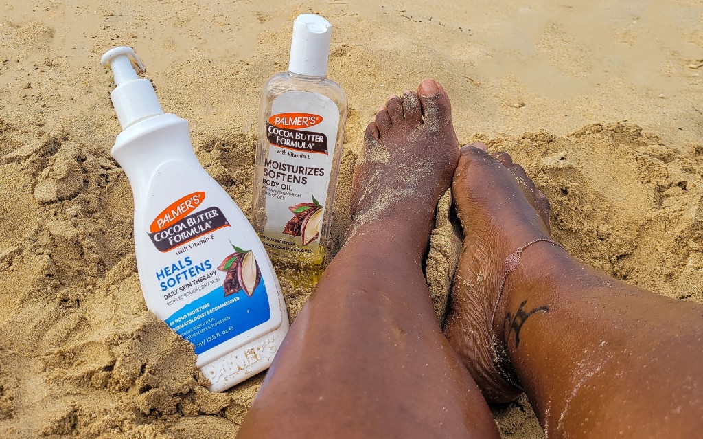 Black woman's legs in the sand with Palmer's Cocoa Butter Lotion and Body Oil, perfect items for your summer skin care routine