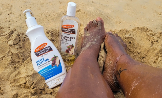 Black woman's legs in the sand with Palmer's Cocoa Butter Lotion and Body Oil, perfect items for your summer skin care routine